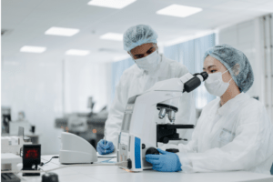 Medical technicians looking into microscope, colleague standing nearby